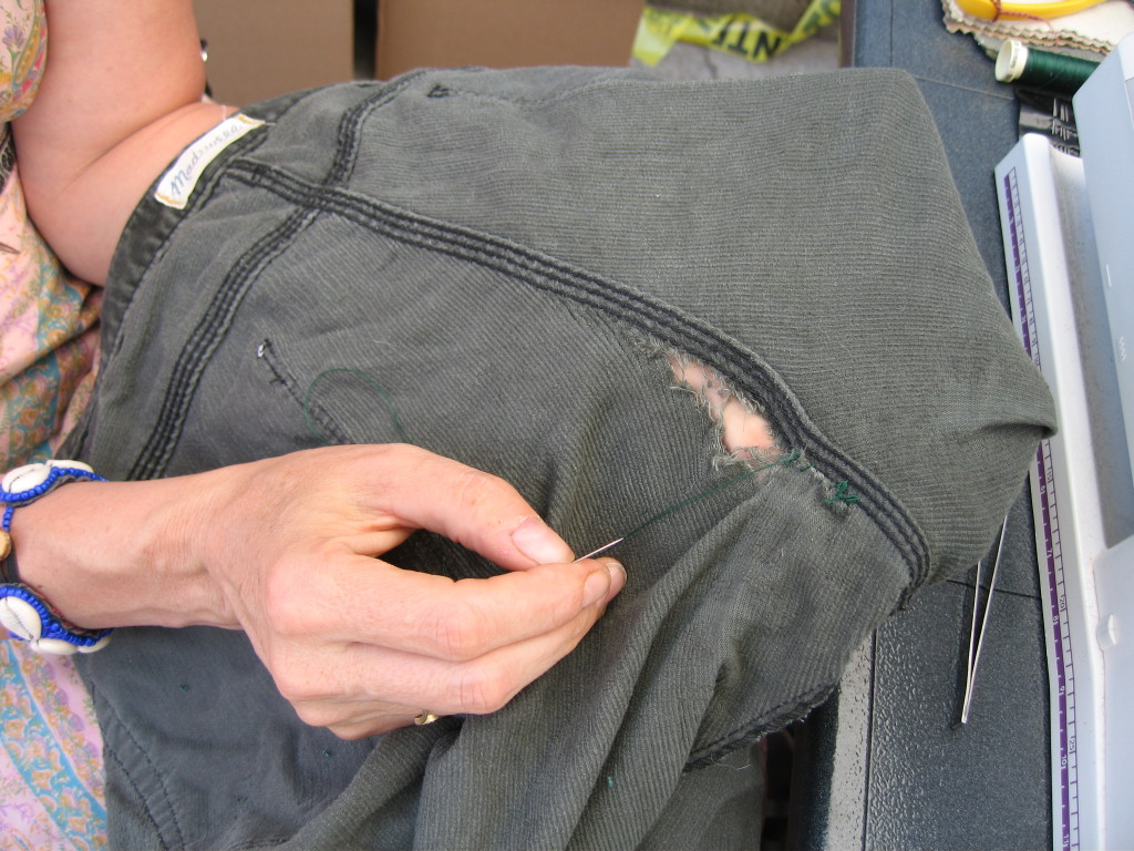Susan, sewing a hole in a pair of pants by hand, before adding a patch over top  for added strength